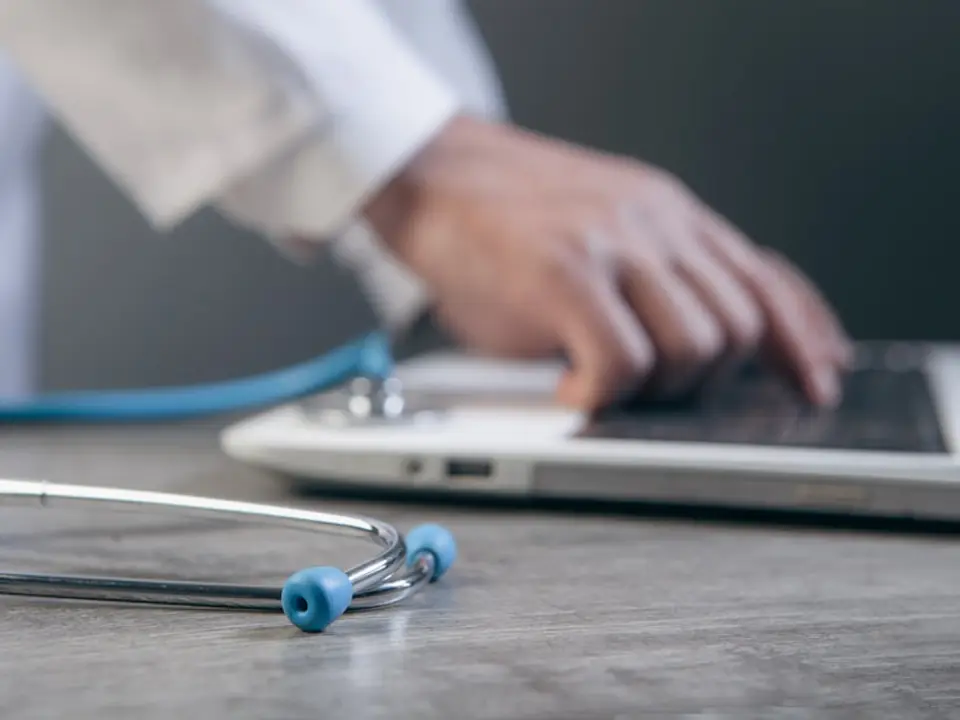 Doctor typing on a laptop with a stethoscope nearby